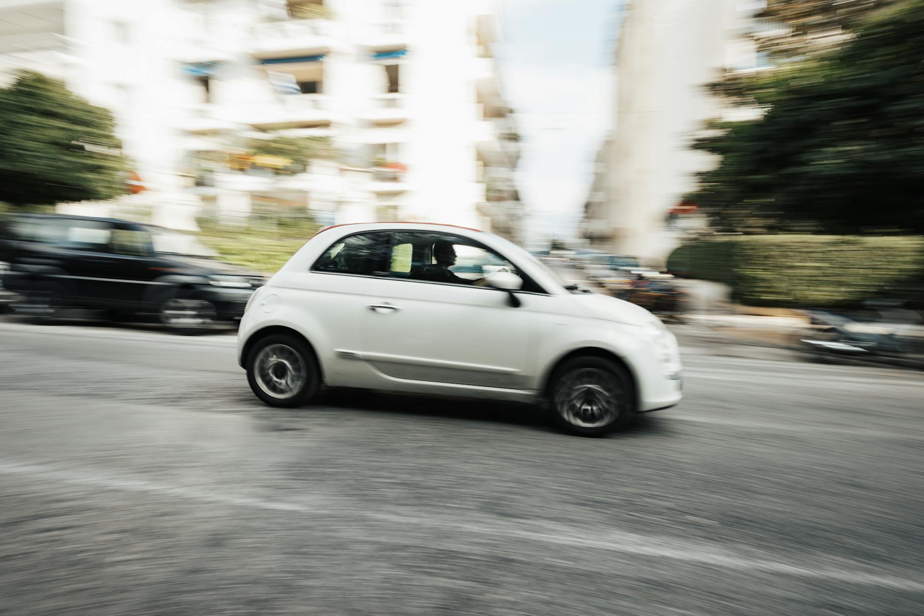 Białe miejskie auto jedzie szybko po ulicy, rozmyte światła miasta