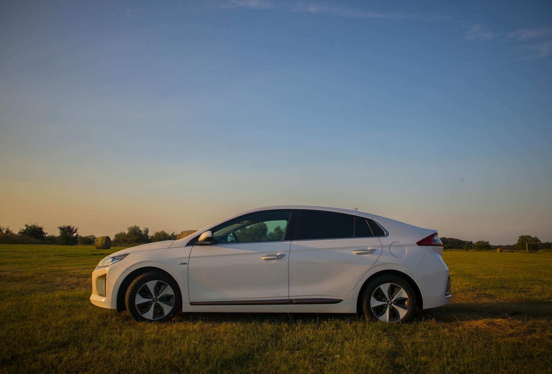 Elektryczny sedan Tesli zaparkowany na polu o zachodzie słońca