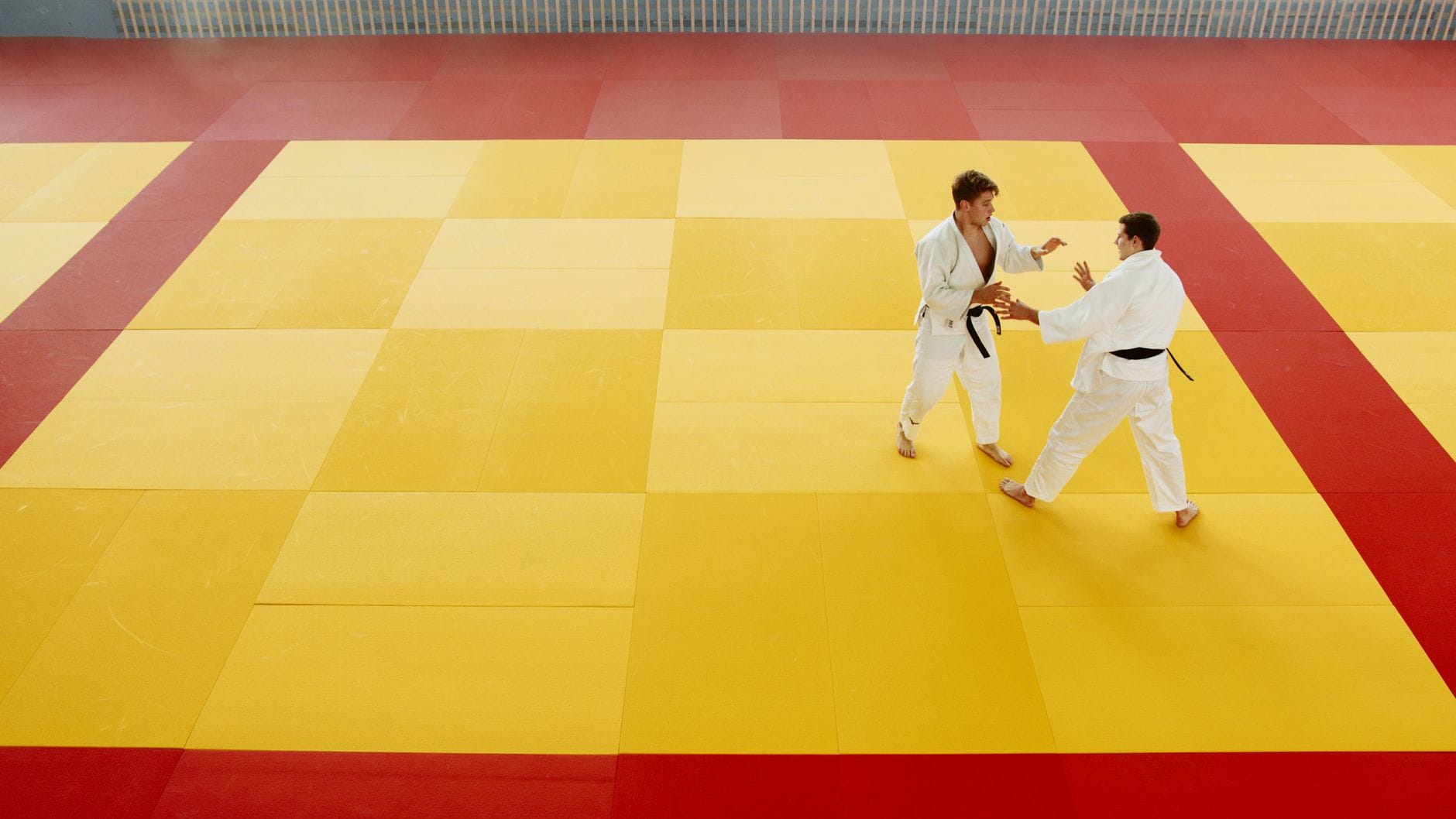 Dwóch aikidoków trenuje techniki na żółto-czerwonej macie w sali