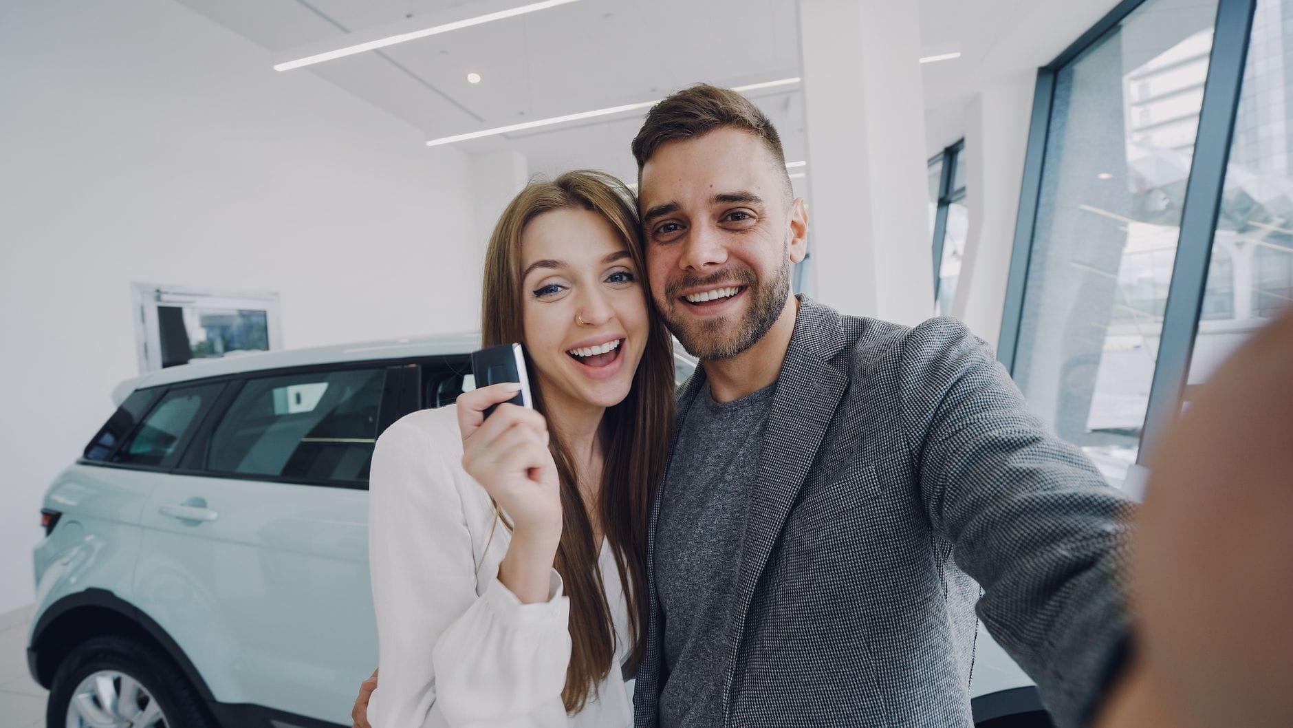Które Mitsubishi wybrać jako pierwsze auto dla młodego kierowcy: omówienie kosztów, ubezpieczenia oraz poziomu bezpieczeństwa Młoda para robi selfie przy nowo kupionym samochodzie w salonie