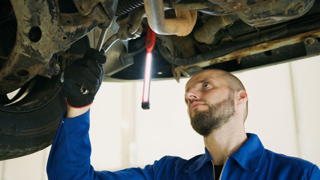 Mechanik wykonujący przegląd auta na podnośniku w warsztacie