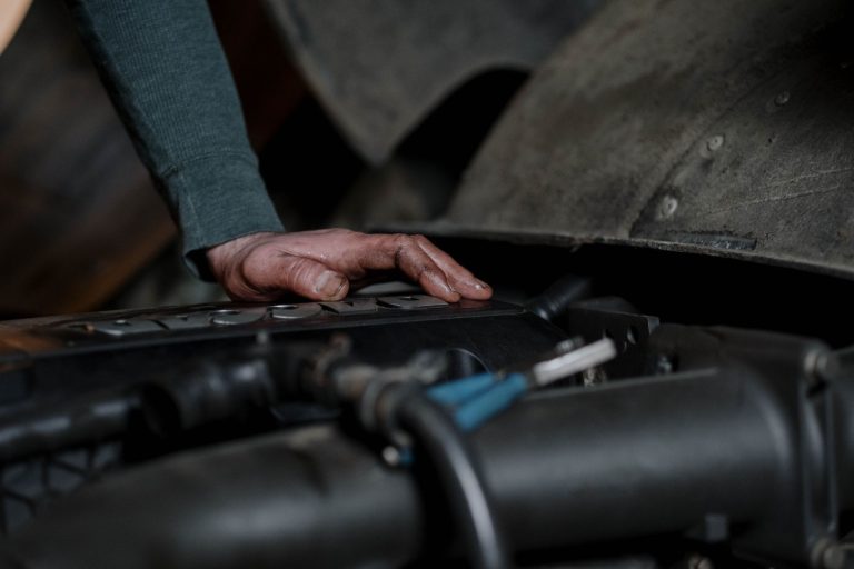 Mechanik z brudnymi rękami sprawdza silnik samochodu w warsztacie